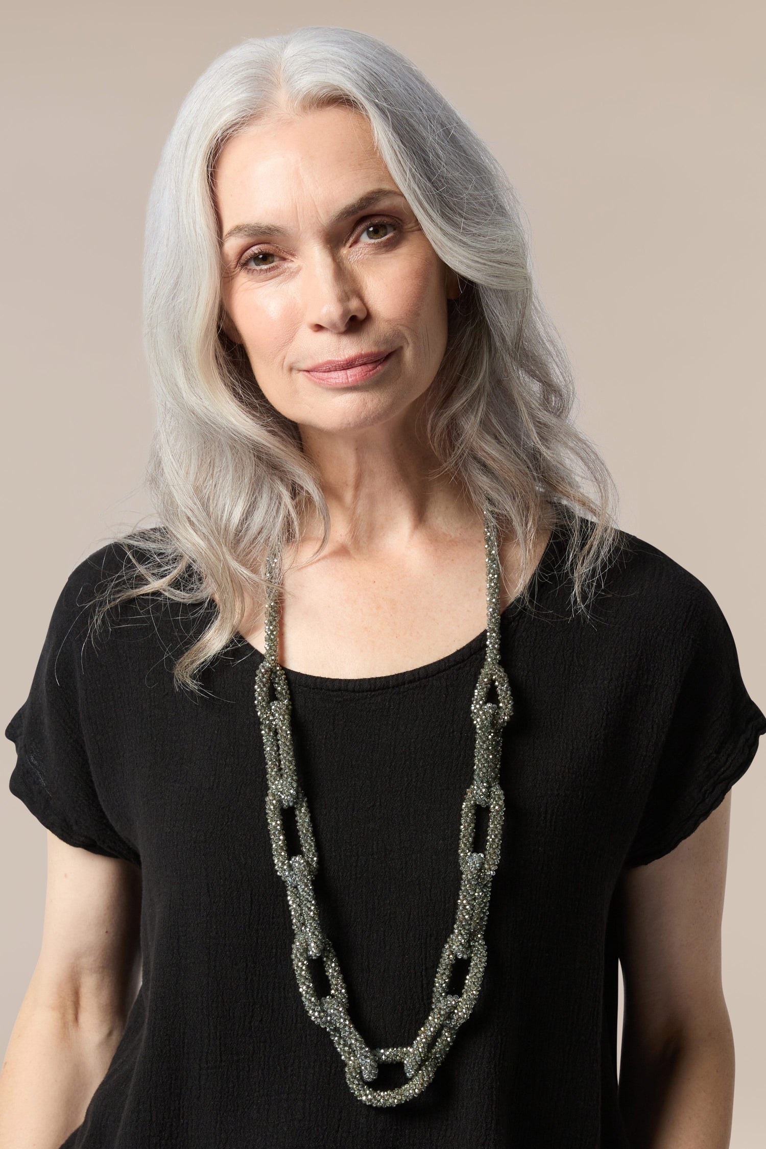 A woman with gray hair wearing a Glacier Necklace, a metallic seed bead necklace.