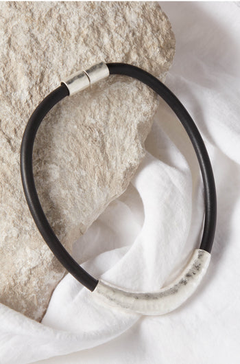 A unique black and silver choker adorned with a silver Hammered Necklace, resting delicately on a rock.