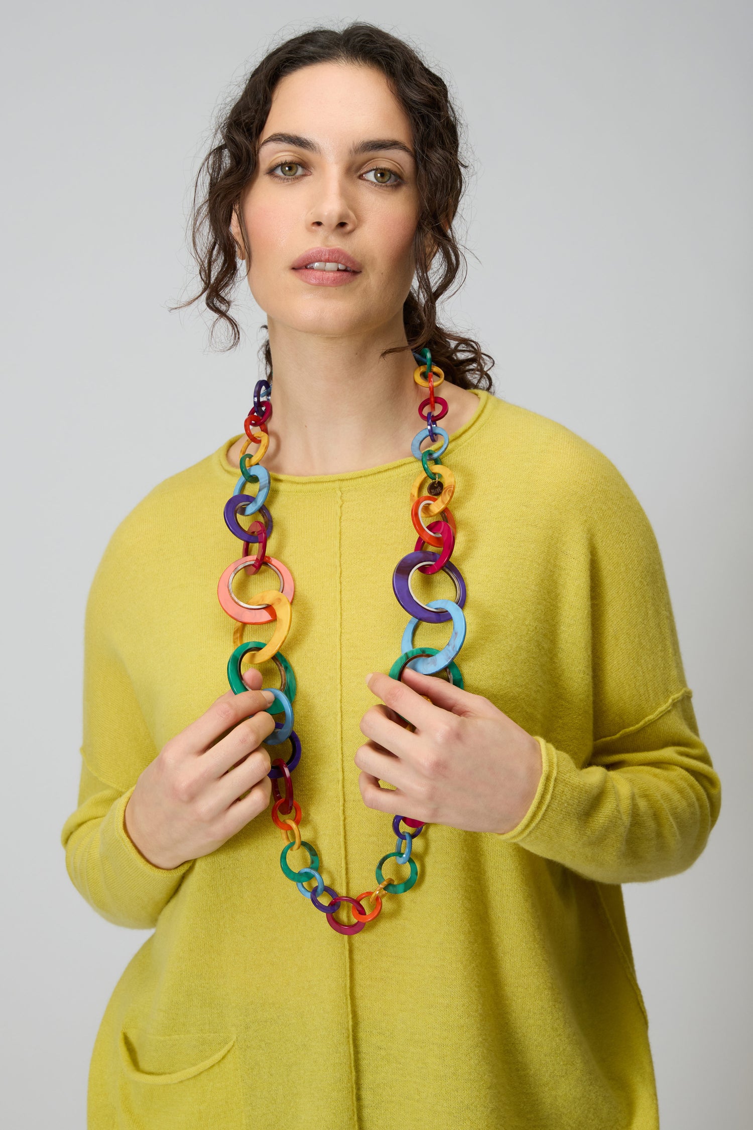 A woman in a yellow sweater wears the Rainbow Resin Hoops Necklace, standing against a plain light gray background.