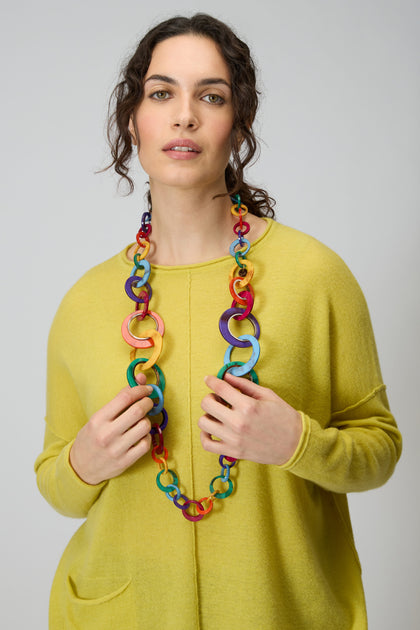 A woman in a yellow sweater wears the Rainbow Resin Hoops Necklace, standing against a plain light gray background.