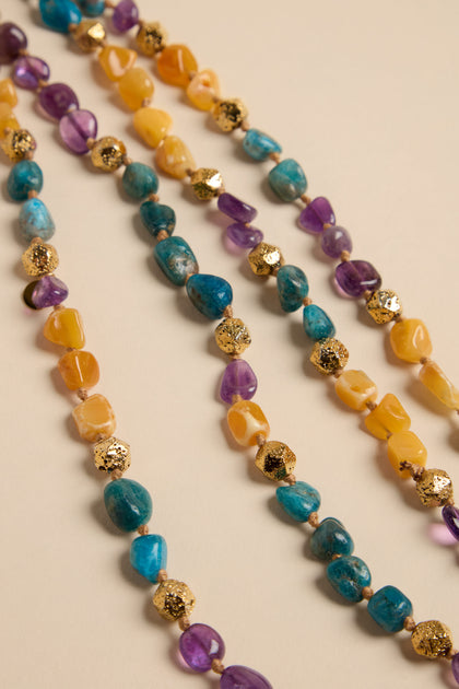 Long Rainbow Bead Necklace featuring three strands of yellow, blue, and purple smooth stones interspersed with small gold textured beads in a repeating pattern.