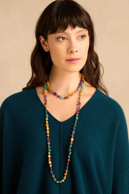 A person wearing a Long Rainbow Bead Necklace featuring multicolored stone beads interspersed with small gold filigree beads.