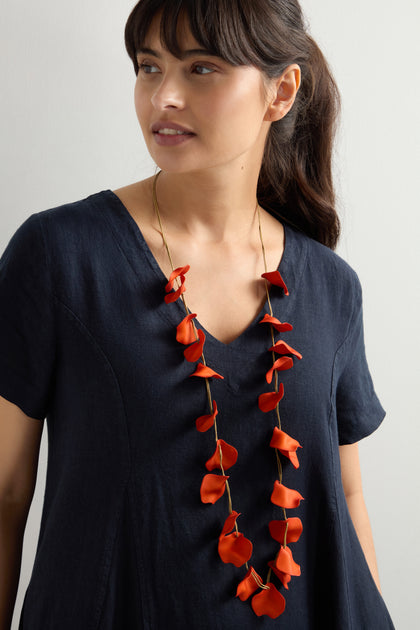 Against a neutral background, a person in a black dress elegantly models the Long Cascade Petal Necklace adorned with coral-hued flower elements.