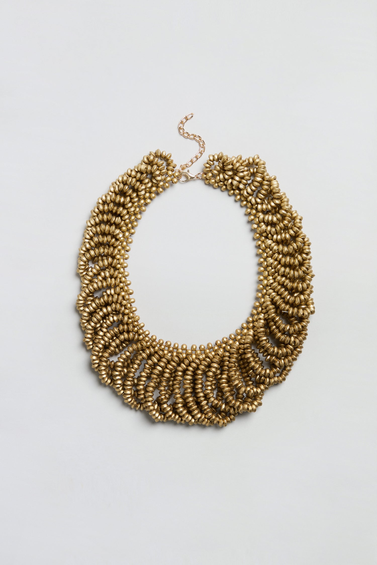 Sure! Here’s the rewritten sentence using your product data: The Gold Beaded Collar Necklace features multiple rows of textured, oval-shaped gold beads and an adjustable chain clasp, beautifully showcased against a plain white background.