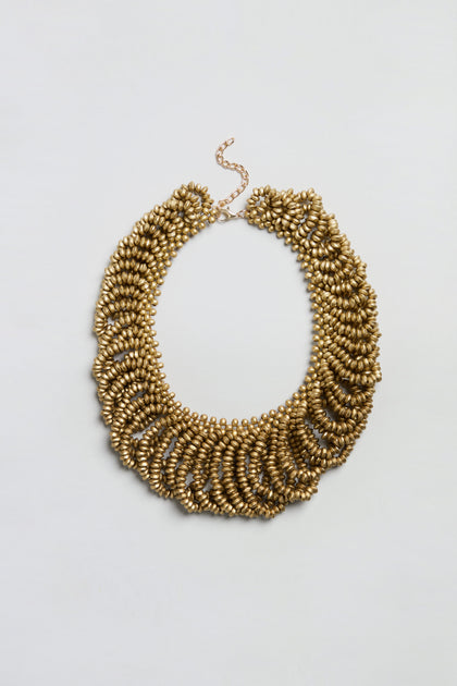 Sure! Here’s the rewritten sentence using your product data: The Gold Beaded Collar Necklace features multiple rows of textured, oval-shaped gold beads and an adjustable chain clasp, beautifully showcased against a plain white background.
