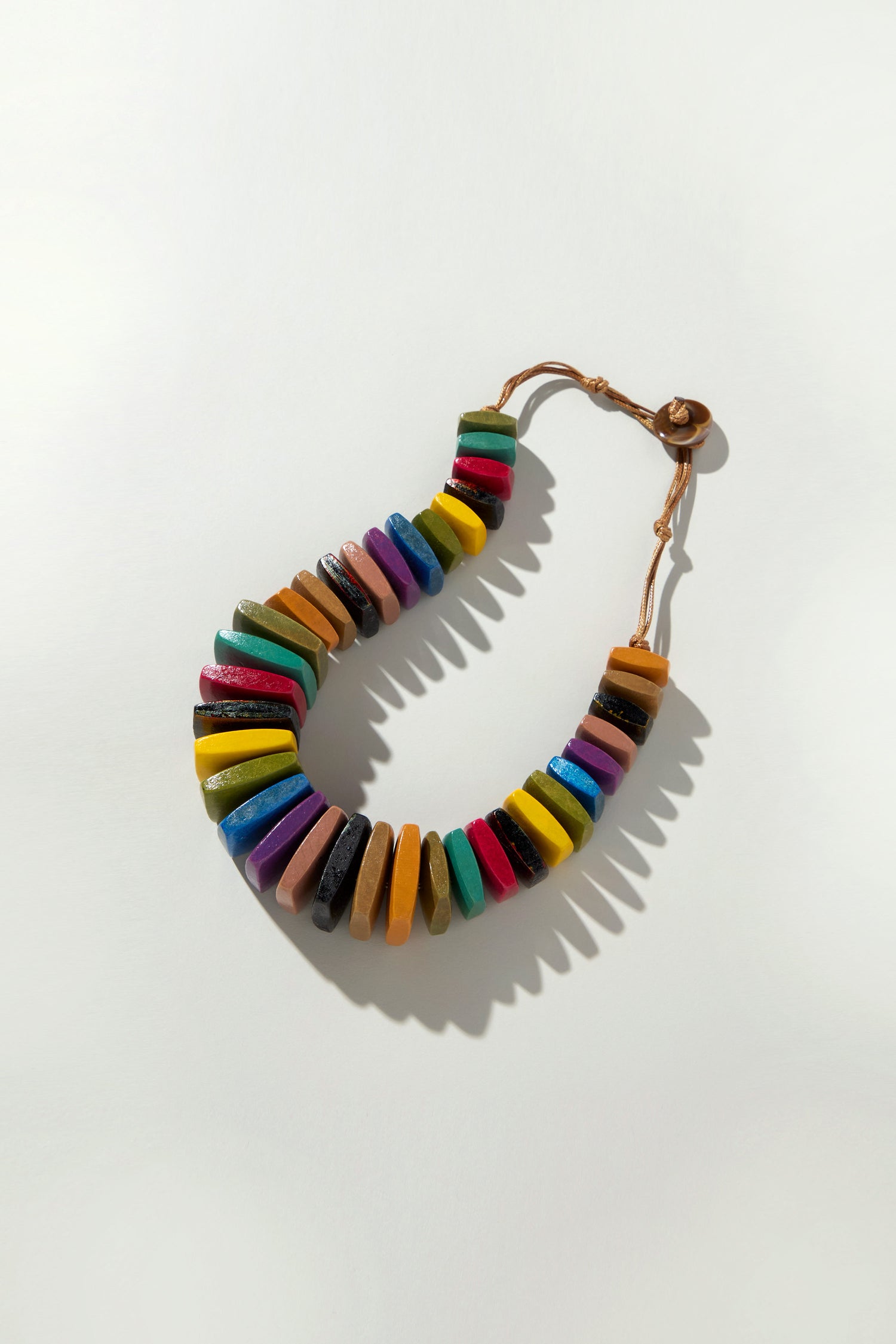 Rainbow Wooden Bead Cord Necklace with Bohemian flair features multicolored flat, rectangular wooden beads on a light background, creating playful shadows.