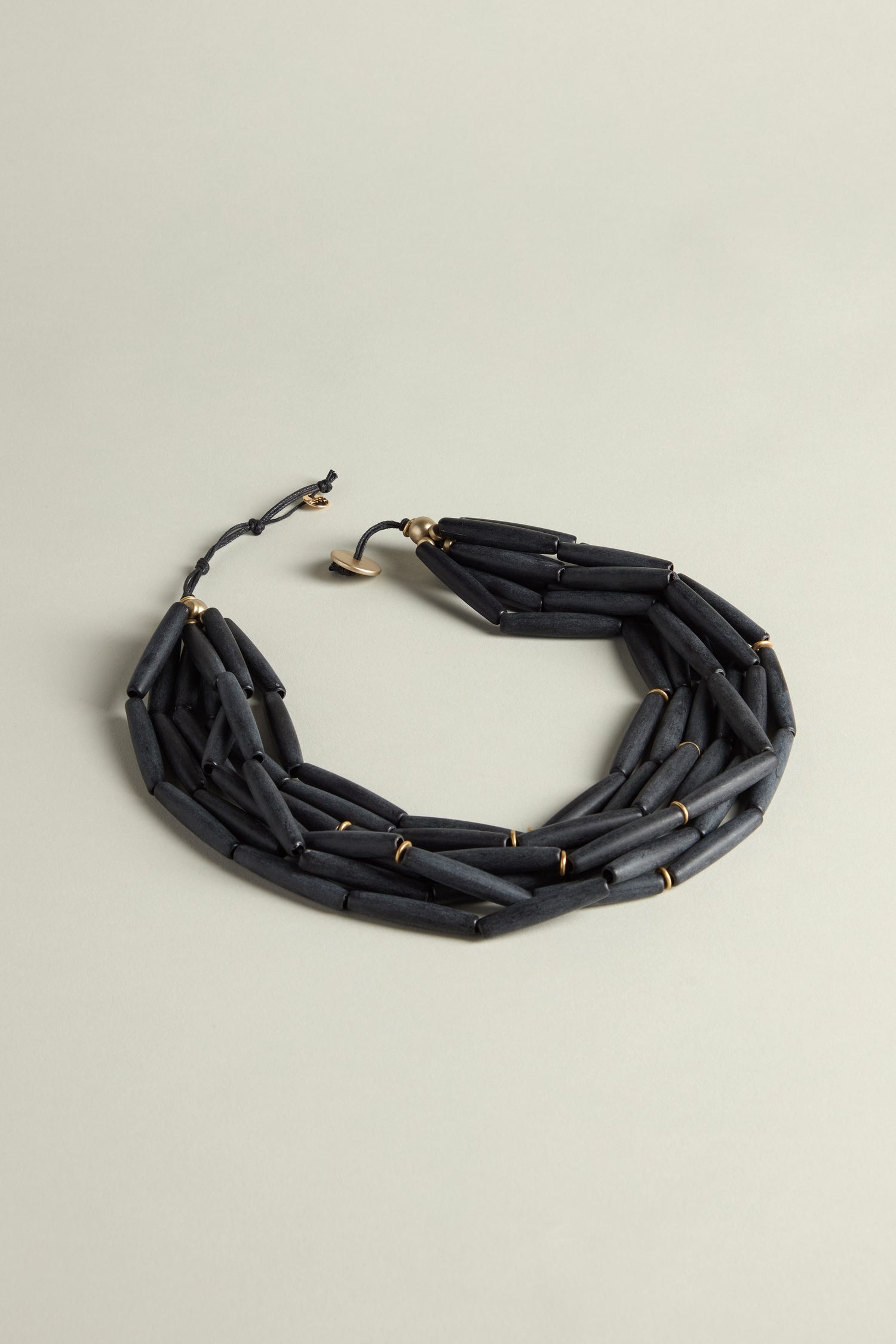 The Noir Cascade Necklace showcases a sleek, minimalist design with matte black beads artfully arranged in several layers against a soft light gray backdrop.