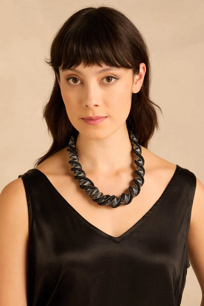 A person wearing the Midnight Helix Necklace, featuring a statement design of coiled, twisted metal in black and metallic silver sections.