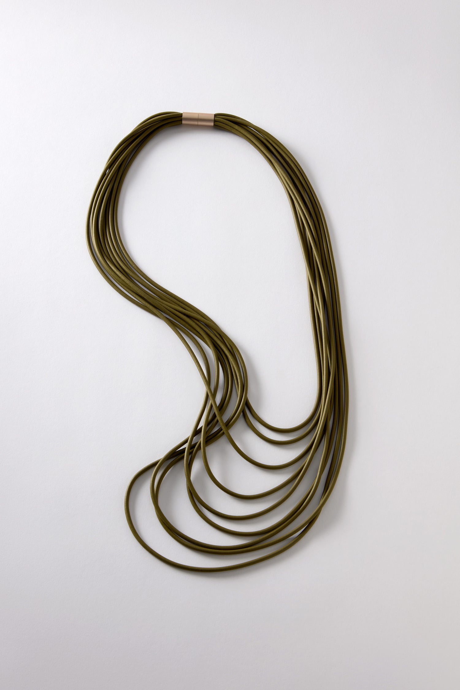 The Khaki Multi Strand Necklace is crafted from olive green rubber cord with a magnetic clasp. This stylish piece showcases a layered overlapping design against a plain background.