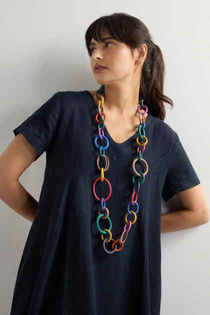 Someone in a plain dark dress performs a playful dance adorned with the Long Rainbow Hoops Necklace, featuring a chunky and colorful design.