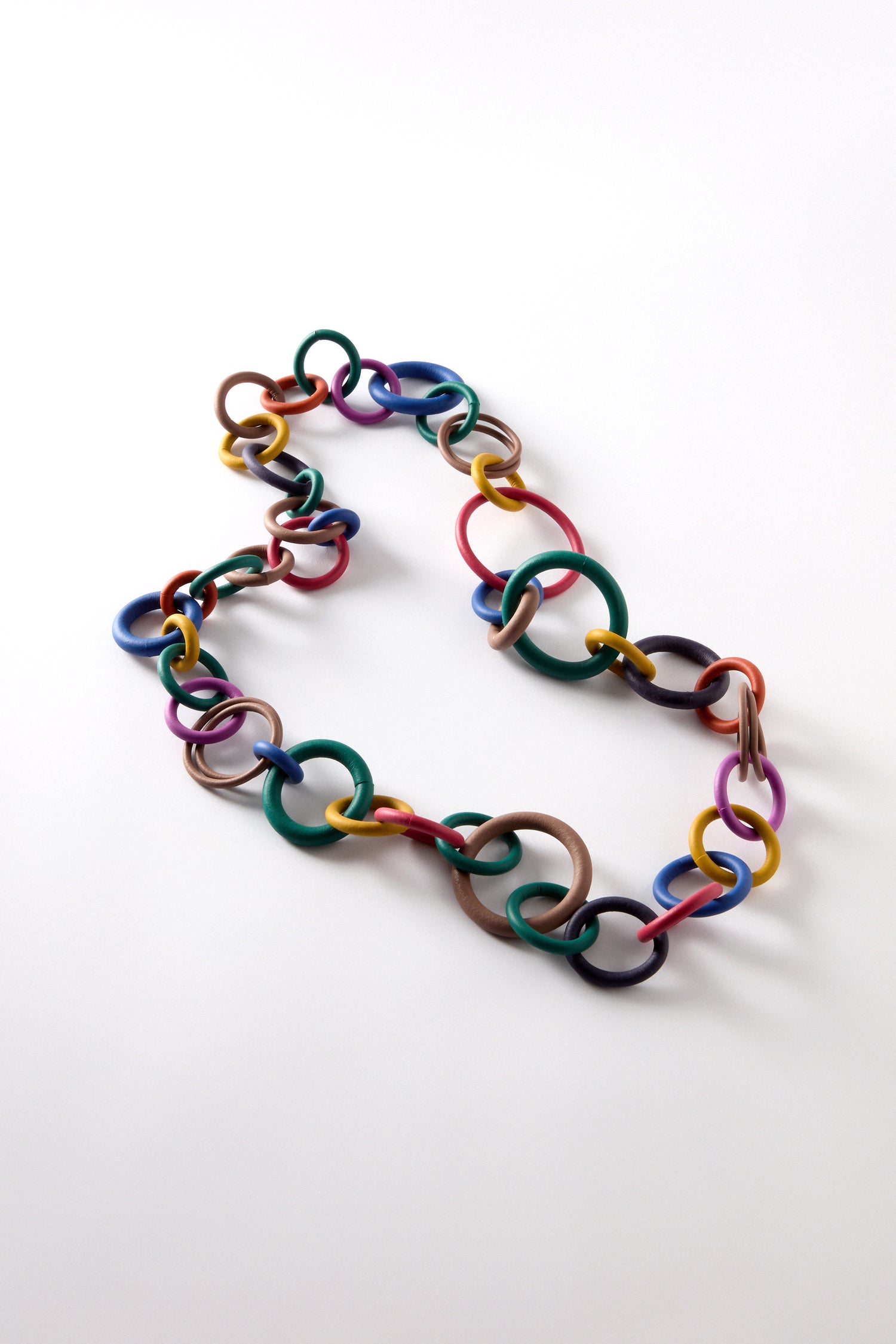 The Long Rainbow Hoops Necklace features a vibrant tumble of playful, interlinked multicolored rings, elegantly arranged on a plain white background.