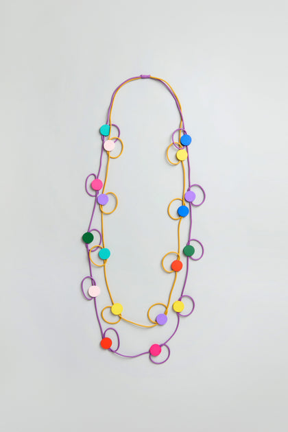 The Rainbow Circle Hoop Necklace features alternating yellow and purple cords with colorful hoops and circles in red, green, blue, pink, orange, and yellow. Lightweight and stylish, it’s ideal for fans of contemporary jewelry.