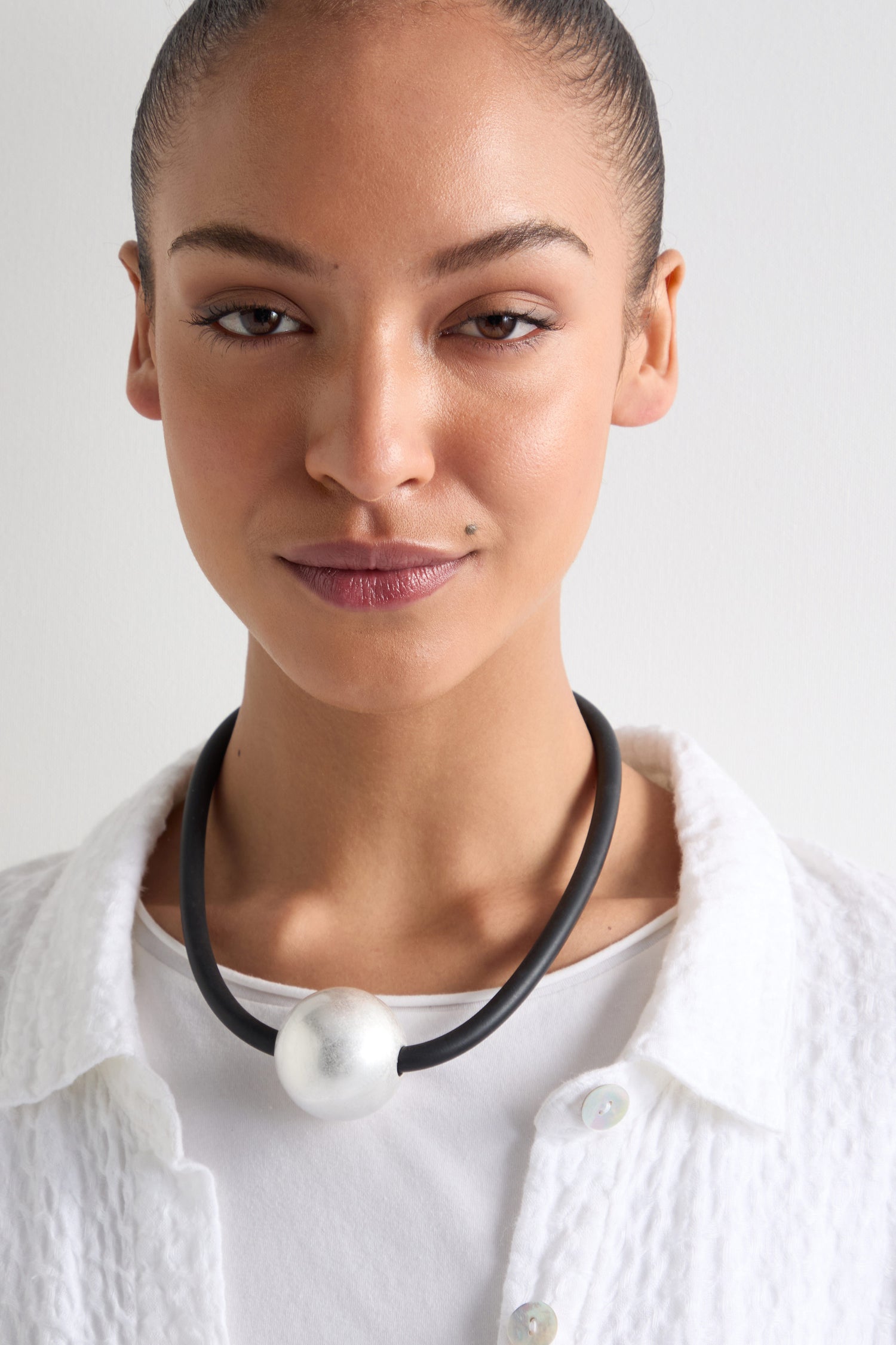 A person in a white textured top wears the Single Sphere Necklace, adorned with a large silver bead, embodying minimalist style.