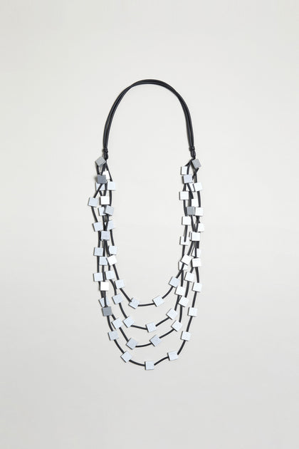 The Cascade Squares Necklace features rectangular silver-tone squares on a black cord, displayed against a plain light background.