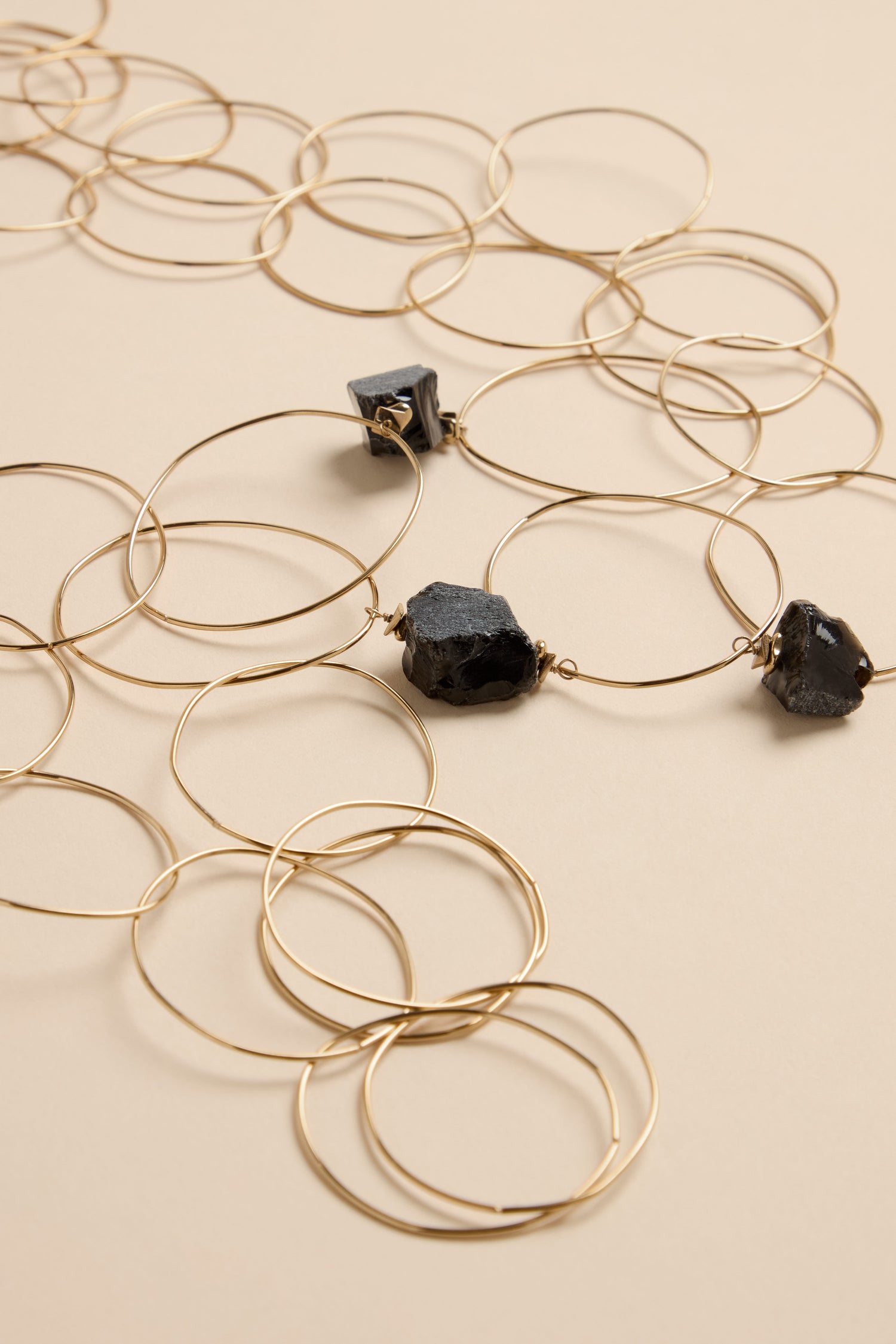 The Midnight Stone Link Necklace features a long chain of thin gold-tone metal rings interspersed with three raw, dark-colored stone accents.