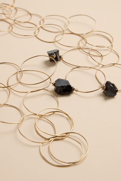 The Midnight Stone Link Necklace features a long chain of thin gold-tone metal rings interspersed with three raw, dark-colored stone accents.