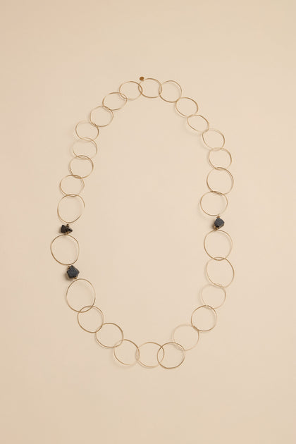 Midnight Stone Link Necklace featuring a long chain of thin gold-tone metal rings accented by three dark, irregular stones.