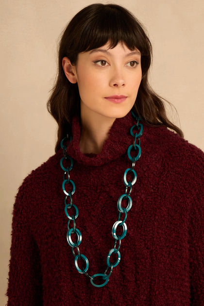 A person wearing a Long Resin Hoop Link Necklace of translucent teal interlocking oval links over a burgundy textured sweater.