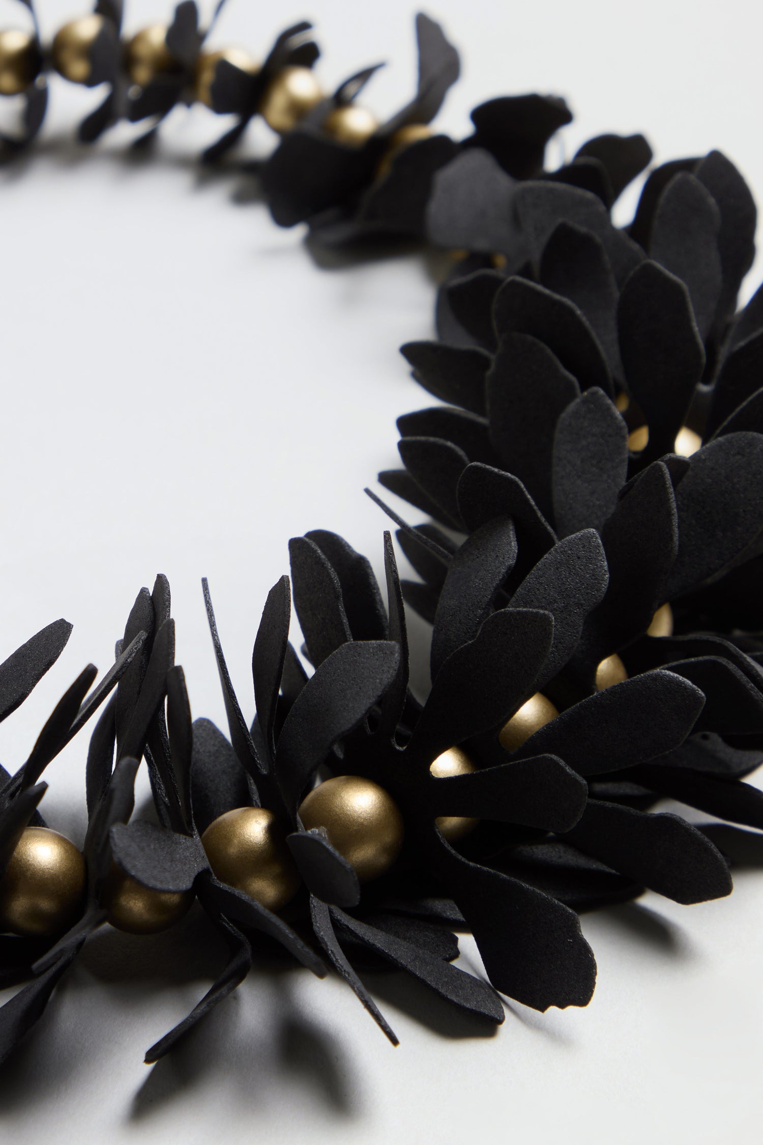 Close-up of the Flower Bead Necklace, featuring black paper leaves and gold accent beads arranged in a circular pattern on a light surface.