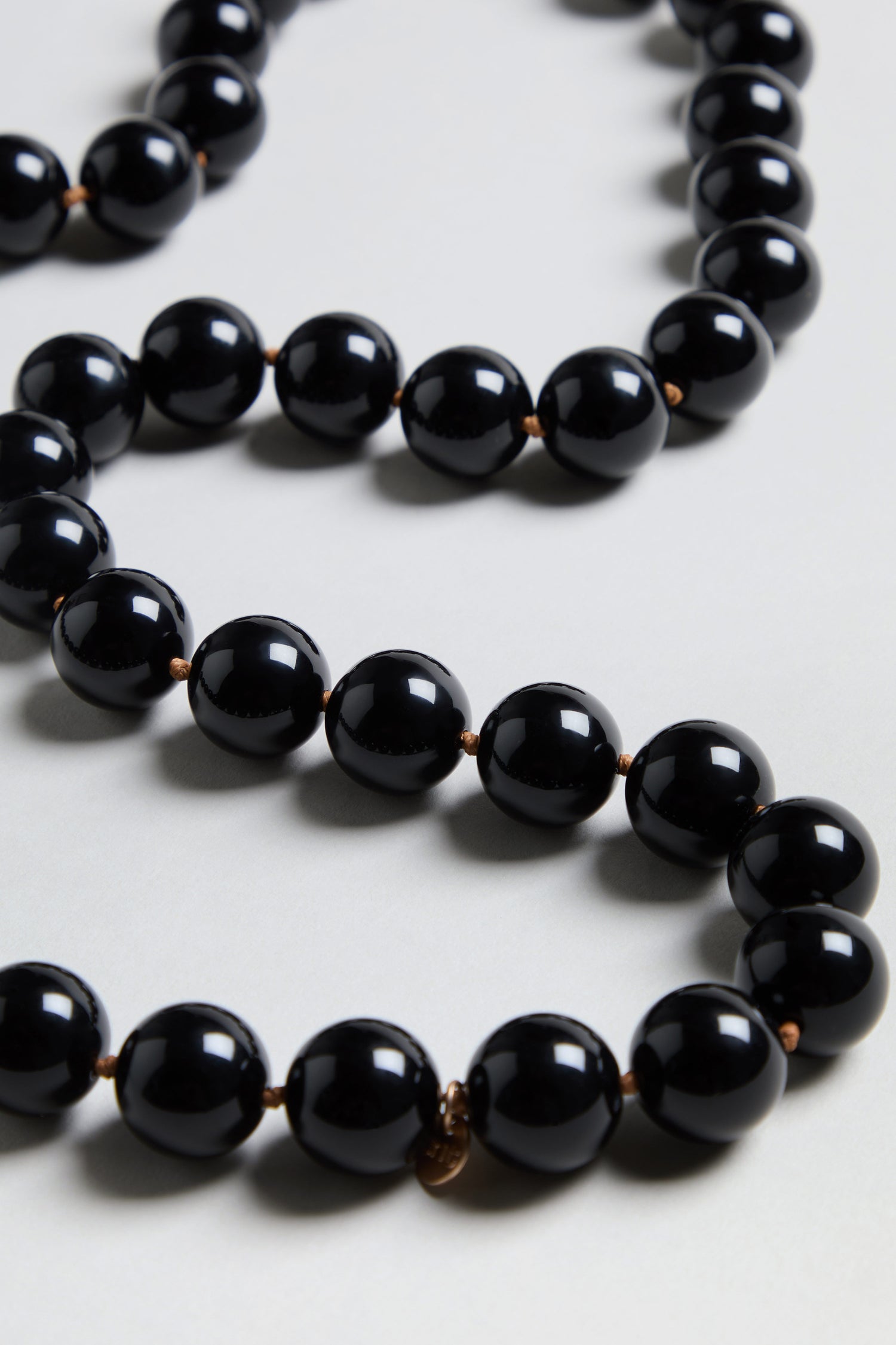 Close-up of the Long Spheres Necklace, showcasing large, glossy black resin beads with a gold burnished finish, each bead carefully knotted between the next and arranged on a light surface.