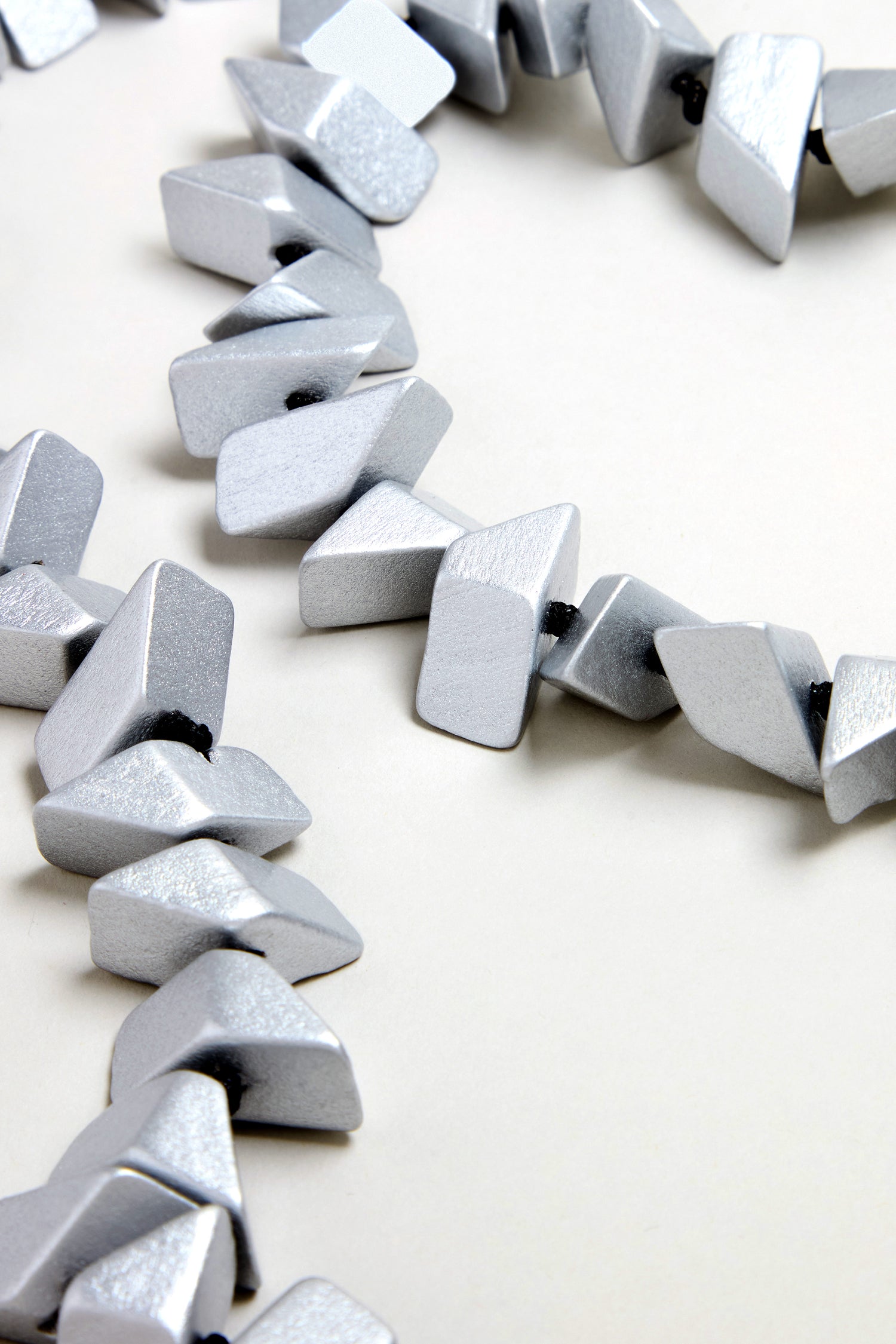 Close-up of the Long Wooden Metallic Necklace, featuring angular silver beads on a light neutral background.