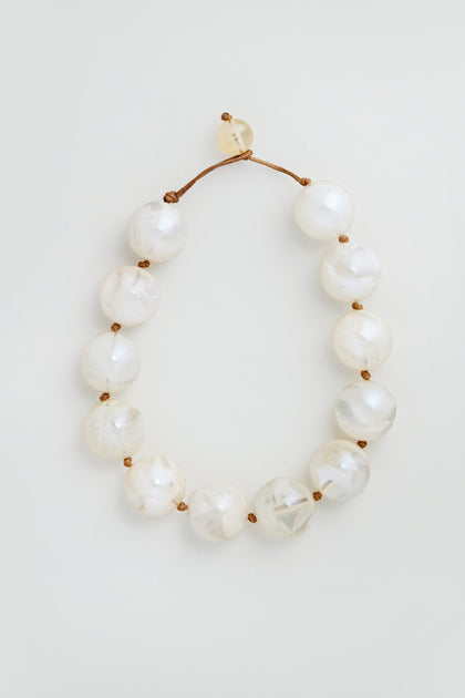 The Marble Spheres Necklace features large, round, marbled white beads strung on a brown cord and is displayed on a light background.