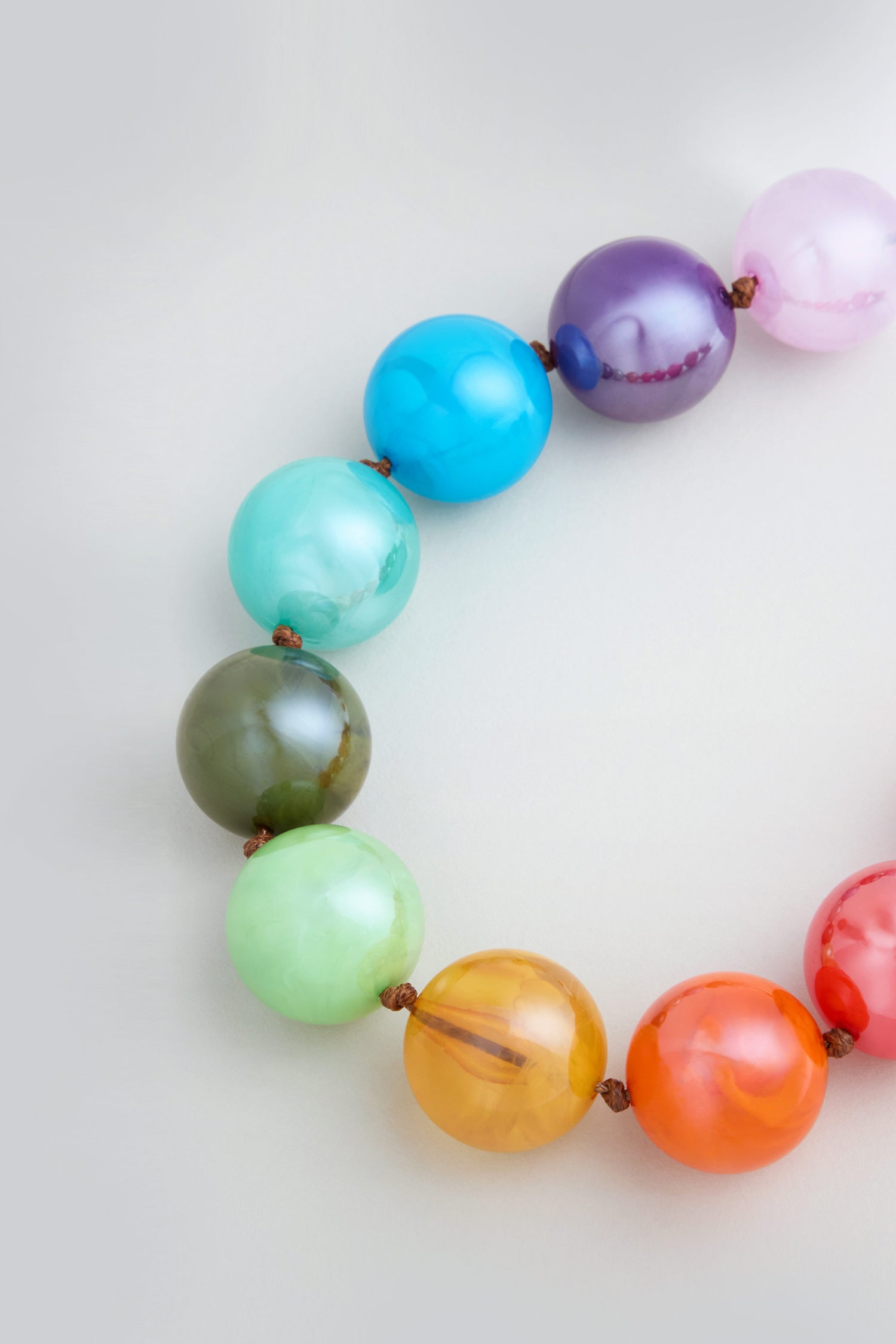A close-up of the Marble Spheres Necklace, arranged in a semi-circle on a light surface, showcasing large, glossy resin beads with a vibrant marbled finish in multiple colors.