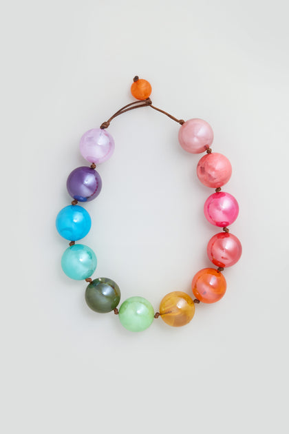 The Marble Spheres Necklace showcases twelve large, round marbled rainbow beads on a brown cord, finished with a loop and bead closure.