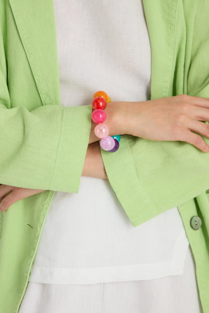 A person with arms crossed, wearing a light green jacket over a white top, showcases the Colour Pop Resin Spheres Bracelet on their wrist.