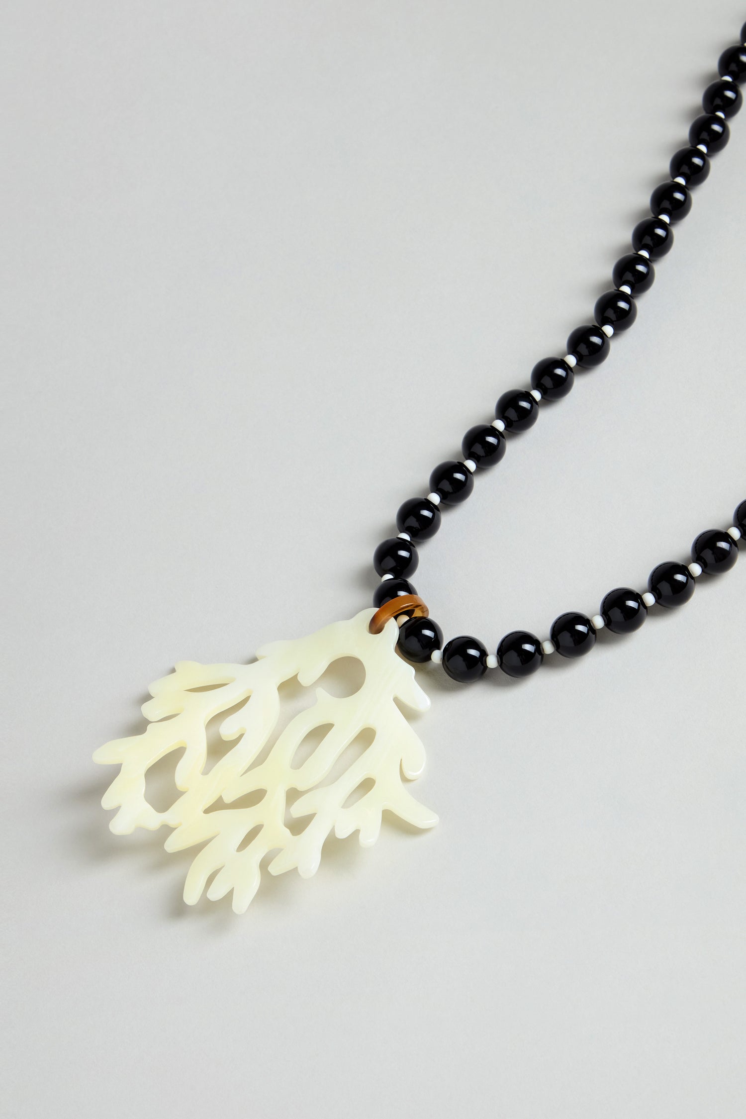 The Coral Resin Pendant Necklace showcases black round beads and a bold white coral resin pendant, set against a light gray background.