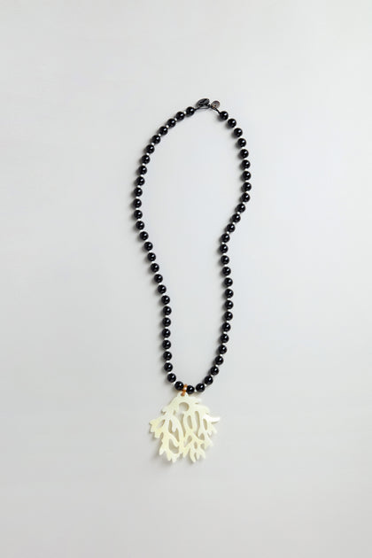 The Coral Resin Pendant Necklace features black beads and a bold white coral resin pendant, shown on a simple light background.
