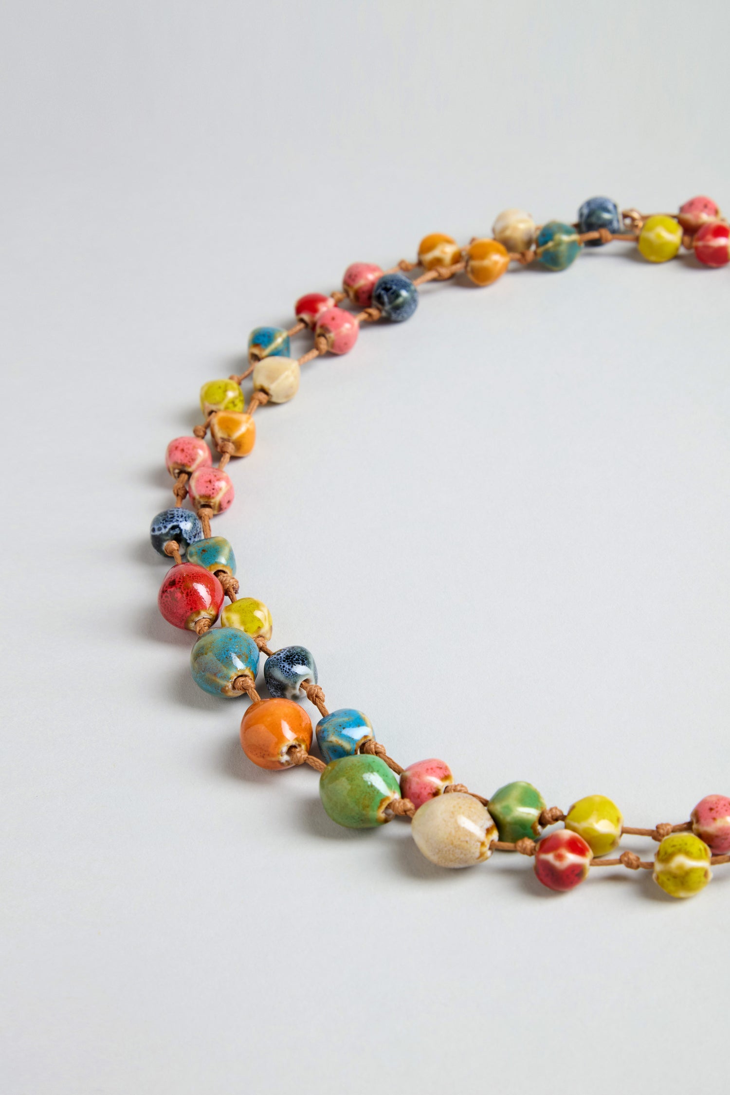 The Rainbow Ceramic Bead Necklace features round, multicolored ceramic beads arranged in a partial circle on a light gray background—perfect for adding playful style.