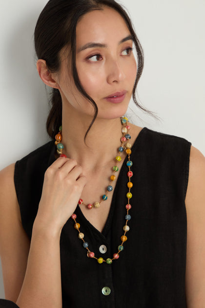 Woman wearing a sleeveless black button-up top and a Rainbow Ceramic Bead Necklace, looking off to the side against a plain background.