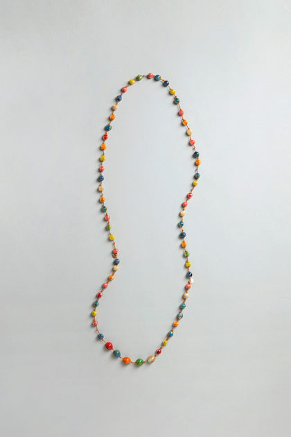 The Rainbow Ceramic Bead Necklace, featuring small multicolored ceramic beads, is displayed in a loose loop on a plain light gray surface.