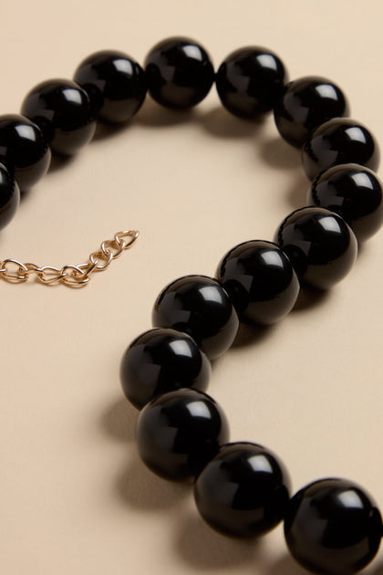 Short Spheres Necklace featuring large, glossy black resin spheres and an adjustable gold-tone metal extender chain.