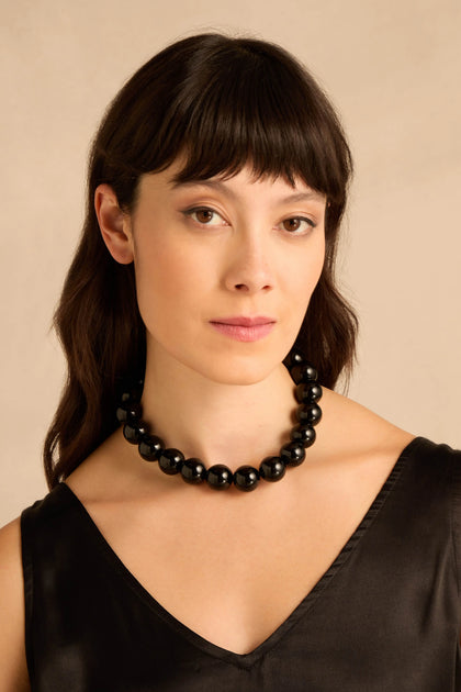 A woman wearing a Short Spheres Necklace made of large, glossy black beads.