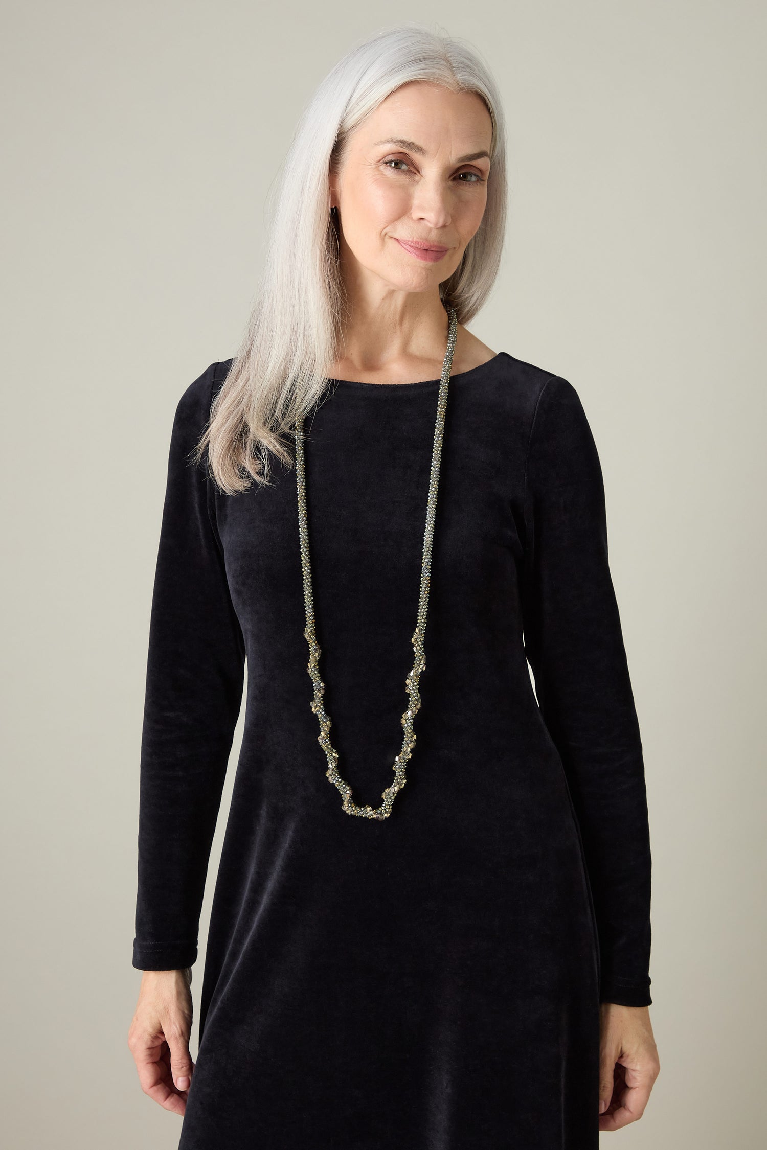 With her long gray hair and black dress, a woman exudes icy elegance, perfectly complemented by the versatile Glacier Spiral Necklace. She stands gracefully against a neutral background.