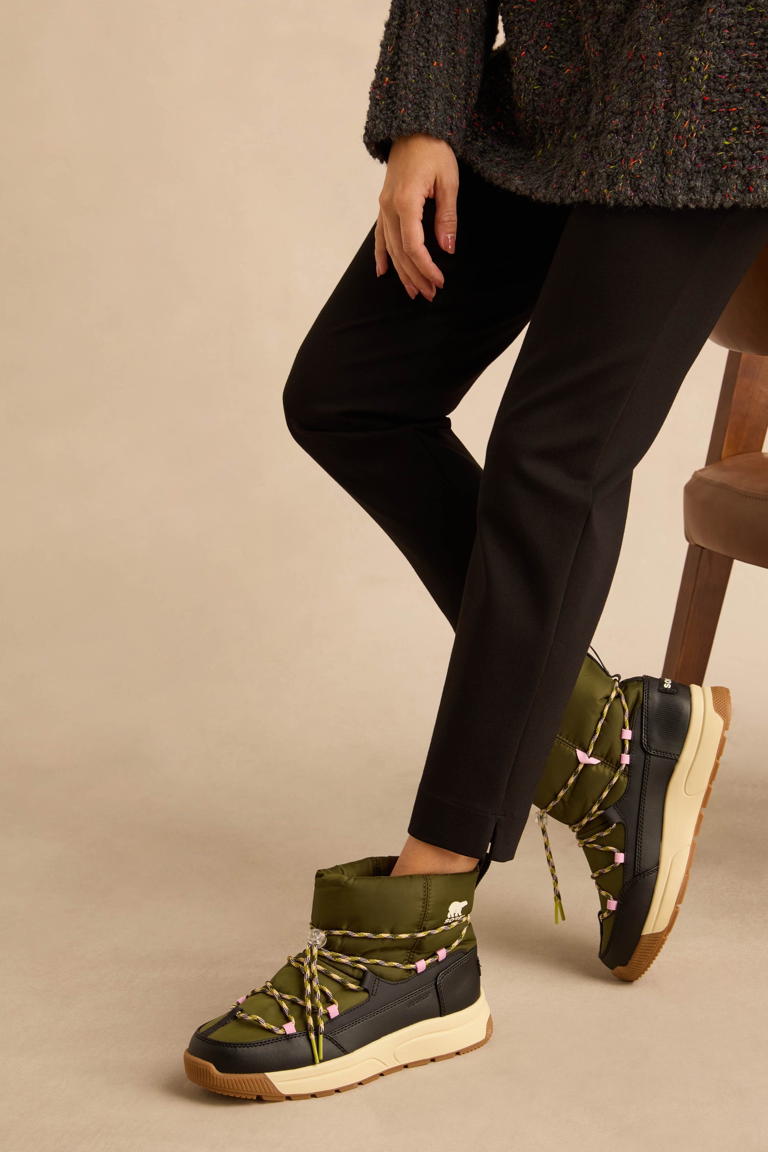 Person wearing black slim-fit trousers and olive green Whitney Quilted Toggle Slip on Boots with toggle lacing and lugged soles.