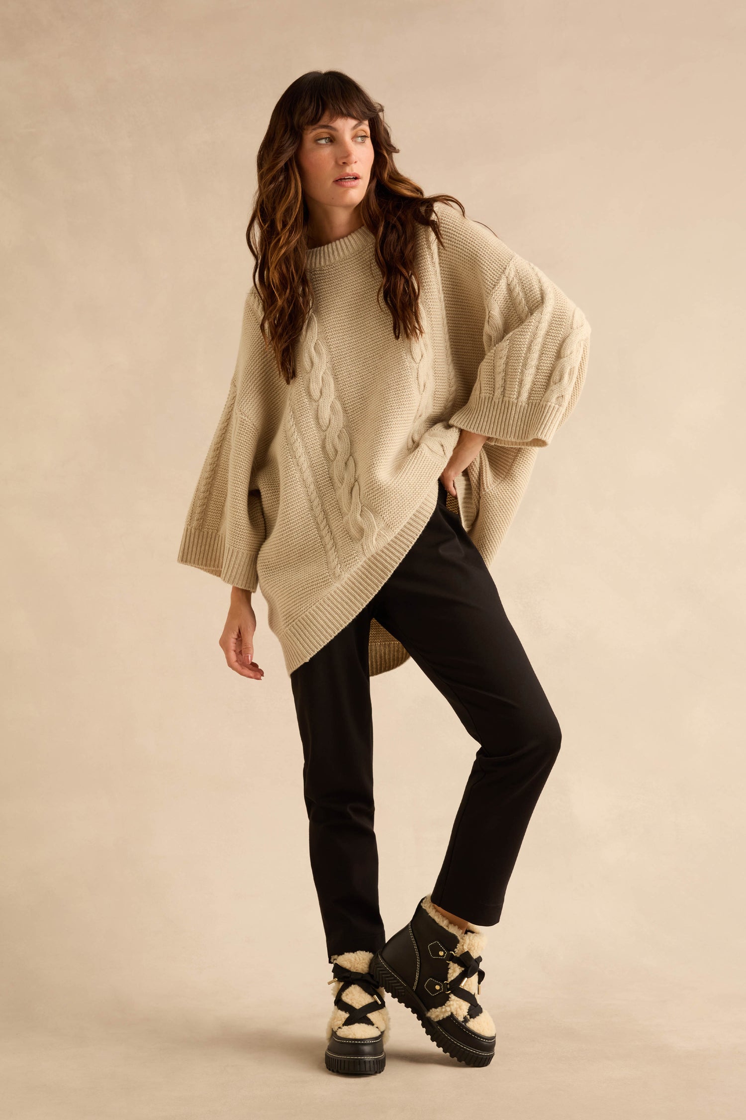 A woman in a beige cable-knit sweater and black trousers wearing waterproof Leather Alpine boots with a shearling tongue and laces.