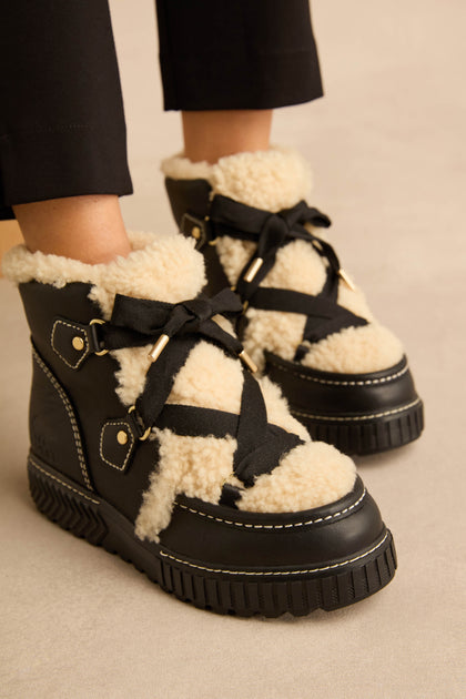Leather Alpine Boots in black with a cream-colored faux shearling tongue, black ribbon laces, and thick rubber platform soles.