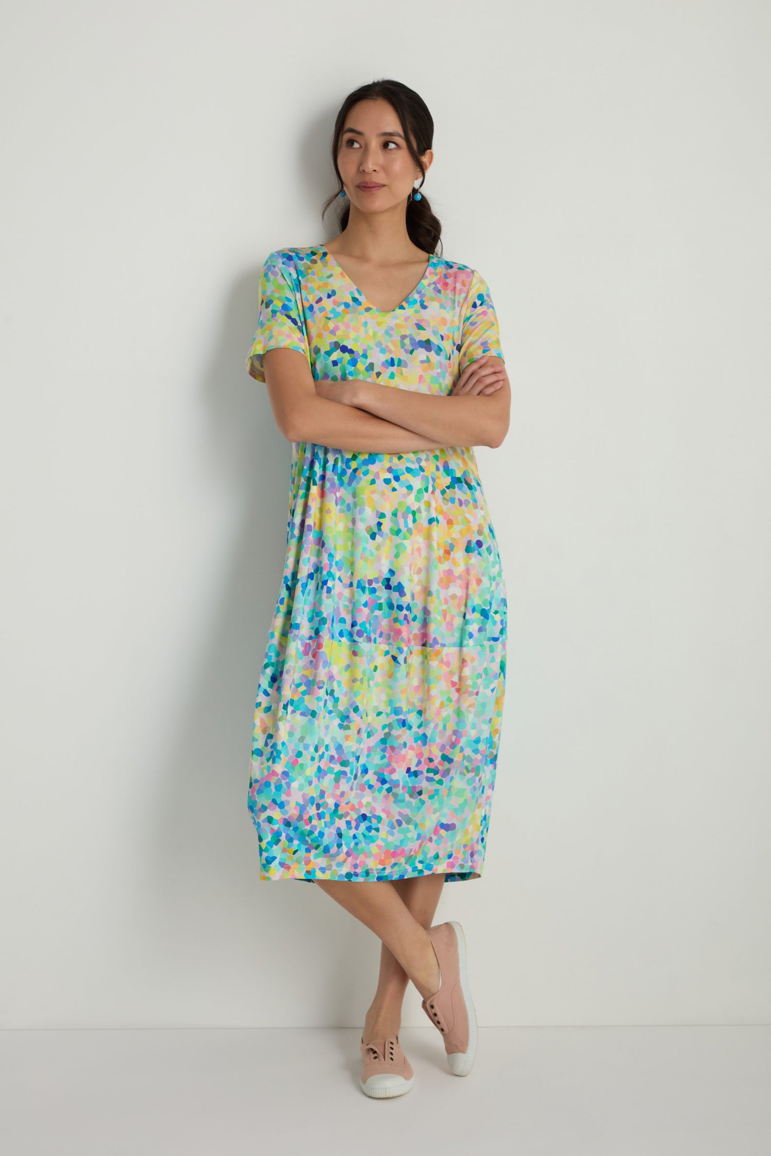 A woman stands with arms crossed, wearing the Summer Confetti Jersey Bubble Dress with short sleeves and light-colored shoes against a plain white wall.
