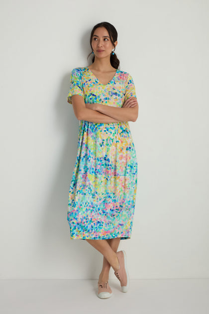 A woman stands with arms crossed, wearing the Summer Confetti Jersey Bubble Dress with short sleeves and light-colored shoes against a plain white wall.