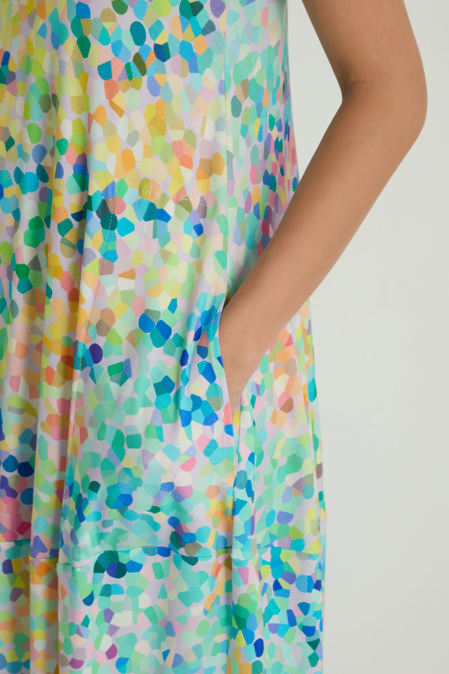 A close-up of a person in the Summer Confetti Jersey Bubble Dress, featuring a colorful abstract pattern, with their right hand tucked into the side pocket.