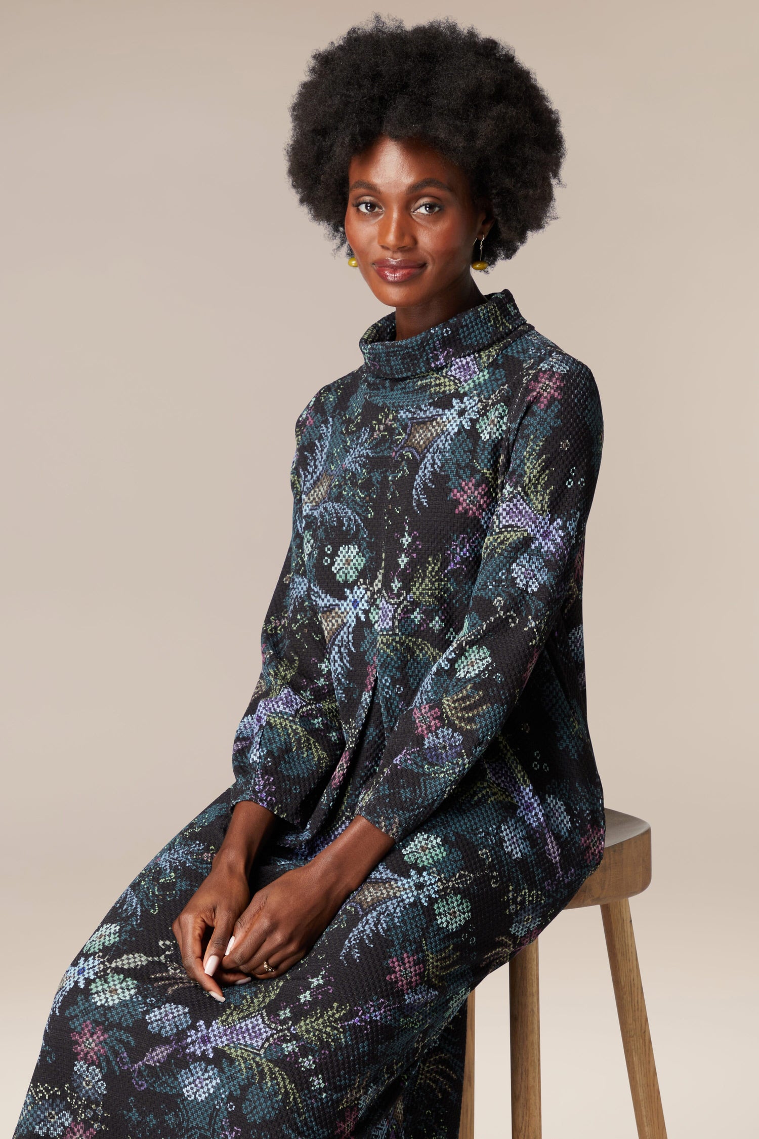 A woman is sitting on a stool wearing the Pixelated Tapestry Jersey Dress.