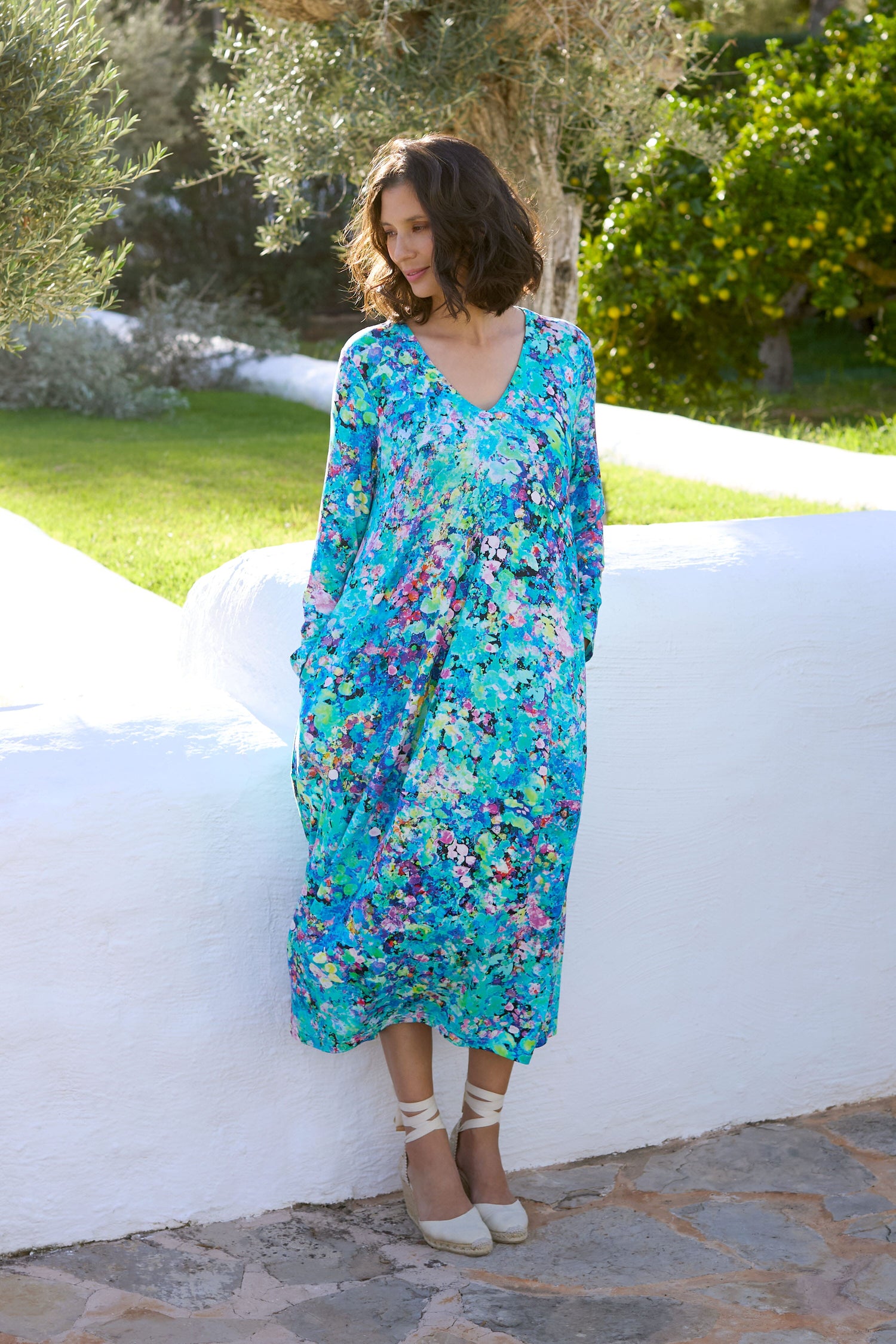 A woman in a blue floral dress leaning against a wall, showcasing the elegance of the Spring Petal Burst Jersey Dress.