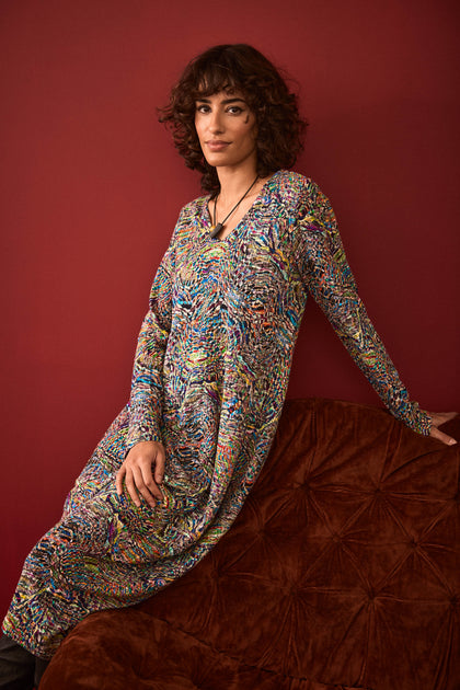 A person with curly hair wearing the Textured Prism Jersey Bubble Dress sits on a brown cushioned couch against a dark red wall.