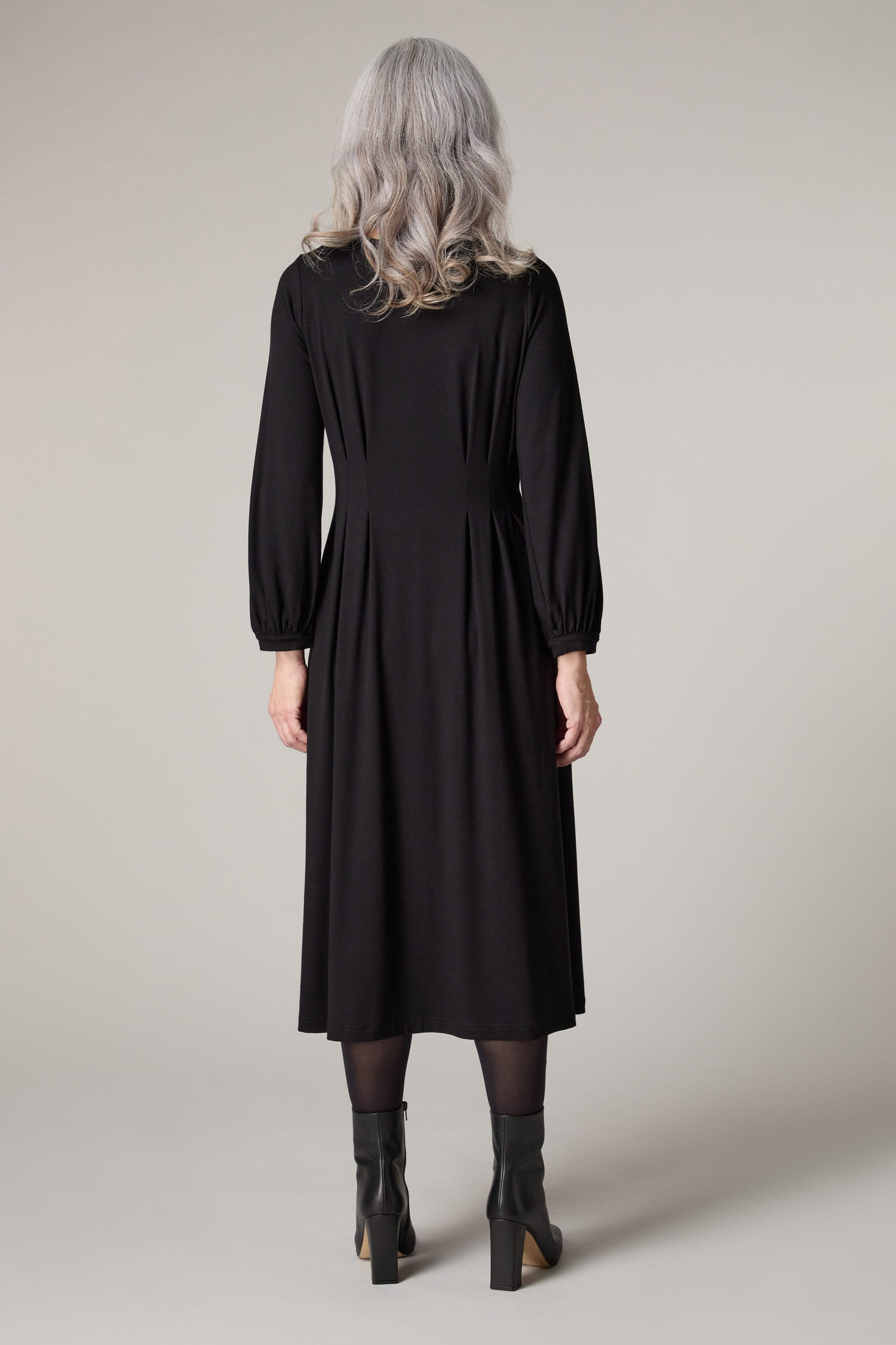 The back view of a woman wearing a Fluid Crepe Pleat Waist Dress with bishop sleeves.