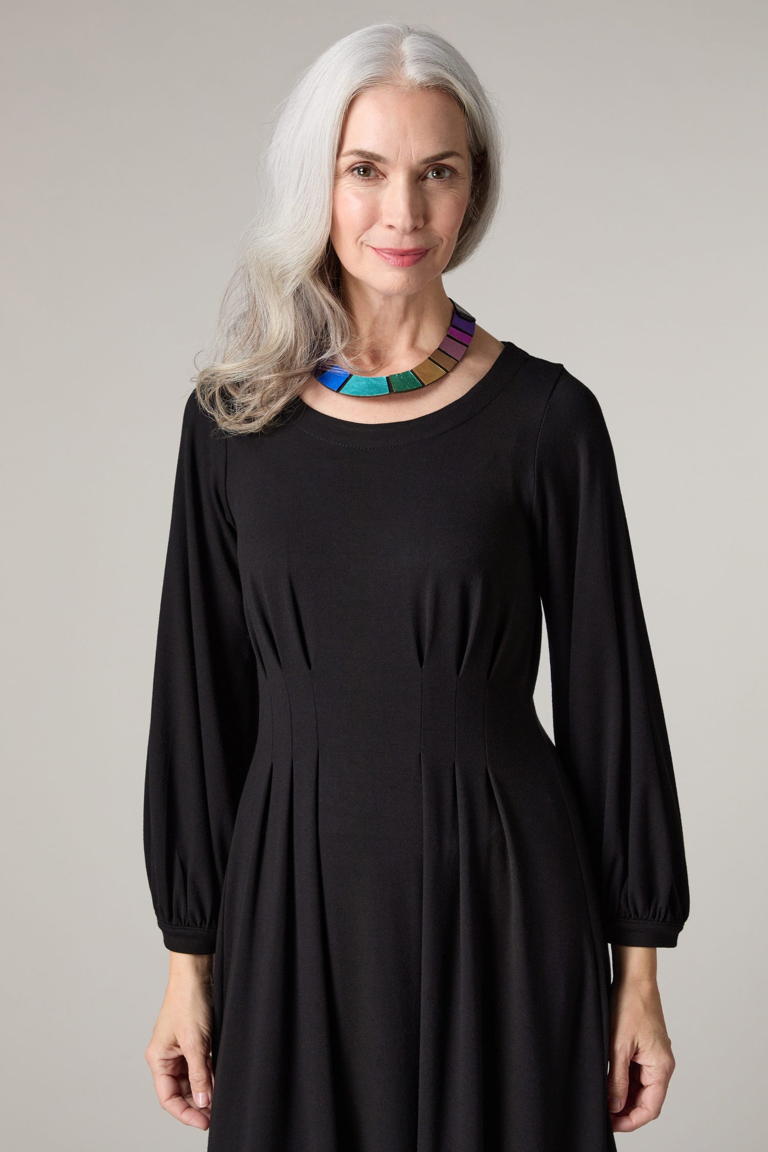 A woman wearing a Fluid Crepe Pleat Waist Dress with a colorful necklace.