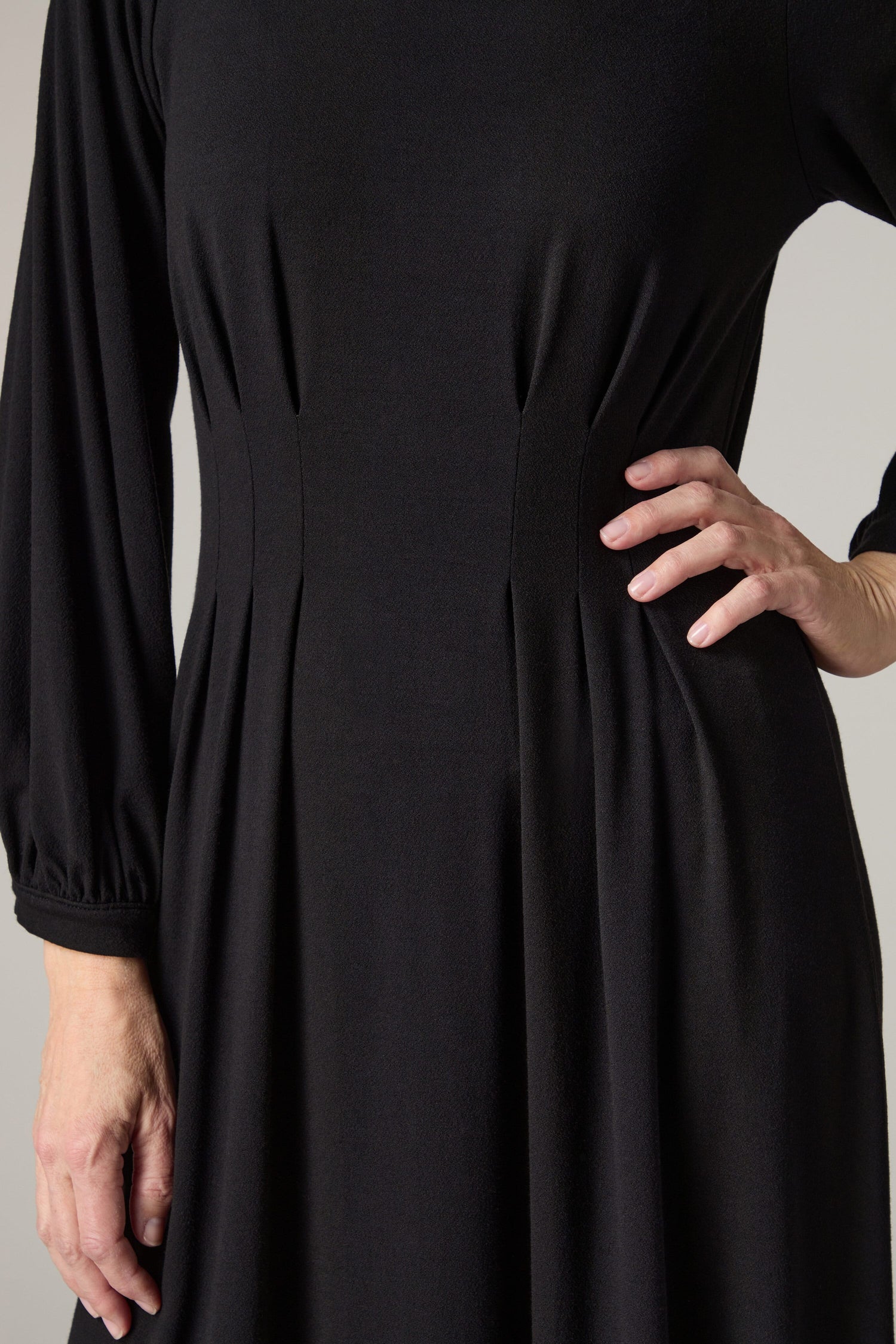 The woman exudes sophistication as she poses in a timeless black dress. The A-line silhouette of this Fluid Crepe Pleat Waist Dress emphasizes her elegance and showcases the Fluid Crepe Pleat Waist Dress's fluid design.