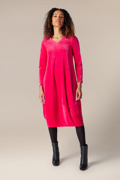 A woman wearing a luxury pink Velvet Jersey Bubble Hem dress and black boots.